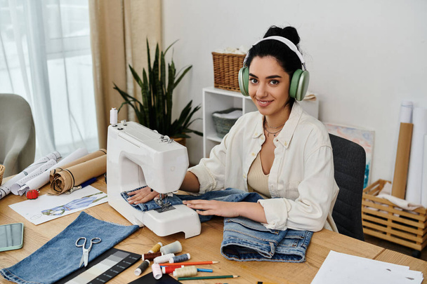 Una mujer joven con atuendo casual se sienta en un escritorio, máquina de coser en acción mientras que upcycling ropa. - Foto, imagen