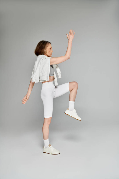 Egy érett vonzó nő fehér rövidnadrágban és fehér felső pózol aktívan és gyakorolja. - Fotó, kép