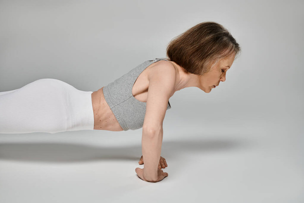 Aantrekkelijke vrouw in comfortabele kleding energiek doen push-ups op witte achtergrond. - Foto, afbeelding