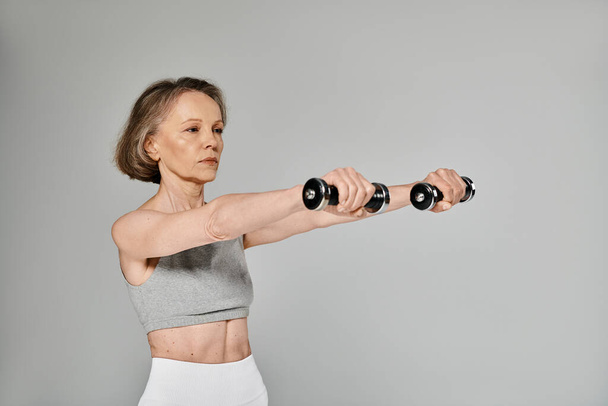 Elderly lady doing dumbbell exercises on gray background. - Photo, Image