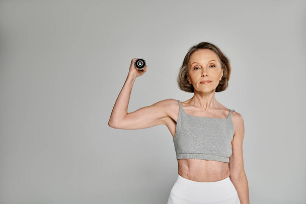 A mature, attractive woman in comfy attire showcases graceful strength while posing with a dumbbell. - Photo, Image