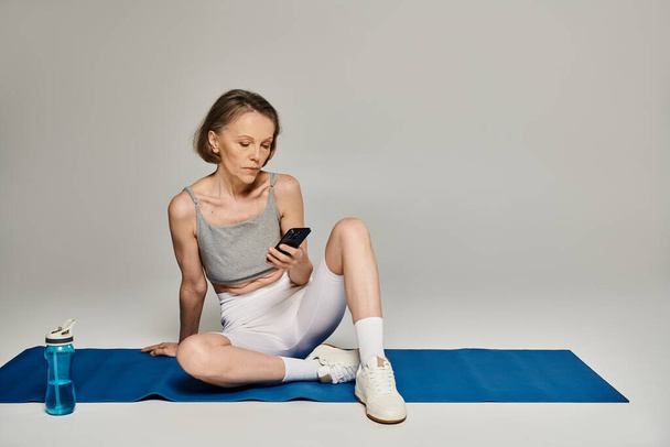 Donna in abbigliamento yoga utilizzando smartphone su tappetino. - Foto, immagini