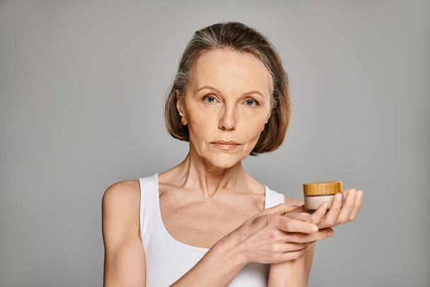 A mature, attractive woman in casual attire holds a container of cream. - Photo, Image