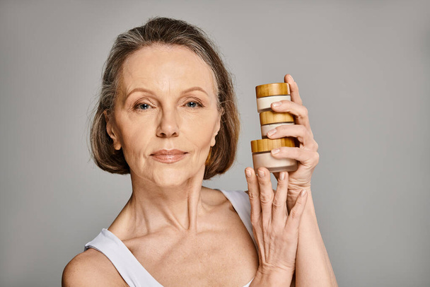 Mujer madura sosteniendo dos frascos de productos para el cuidado de la piel. - Foto, Imagen