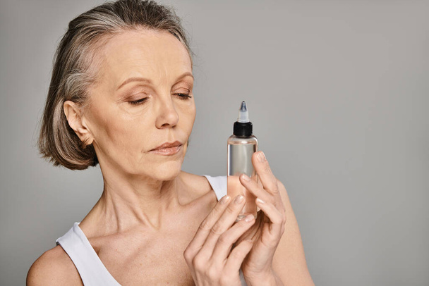 A mature woman gracefully holds a skin care product bottle. - Photo, Image