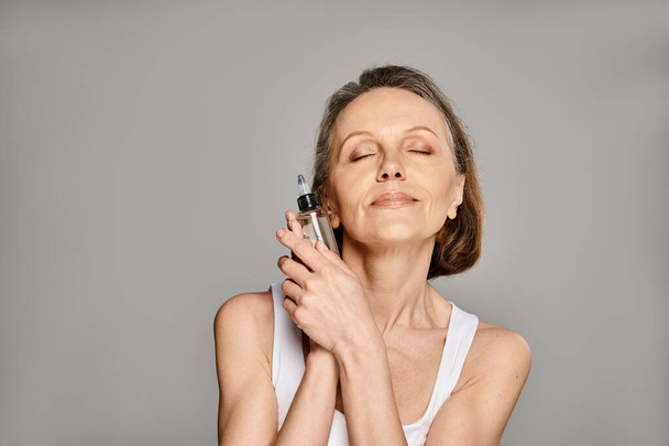 Woman in casual wear peacefully holding serum with closed eyes. - Photo, Image
