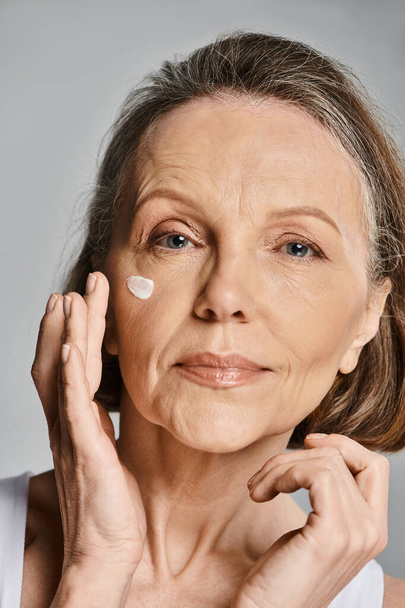 Элегантная пожилая женщина мягко наносит крем на лицо. - Фото, изображение
