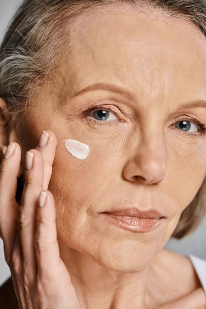 Egy elegáns, idősebb nő finoman krémet tesz az arcára, ápolja a bőrét.. - Fotó, kép