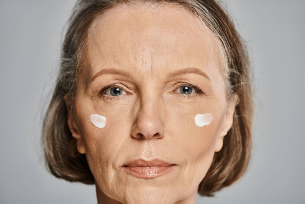 Зрелая женщина изящно обнимает успокаивающие эффекты крема для лица. - Фото, изображение