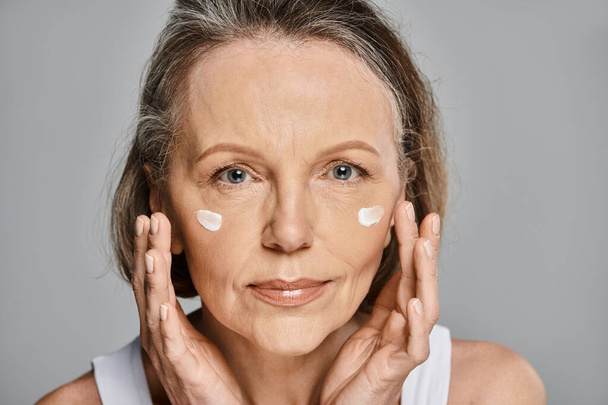 Una mujer mayor aplicando serenamente crema en su cara. - Foto, imagen