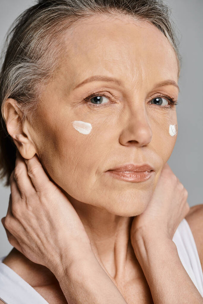 A mature, attractive woman in comfy attire applying cream to her face. - Photo, Image