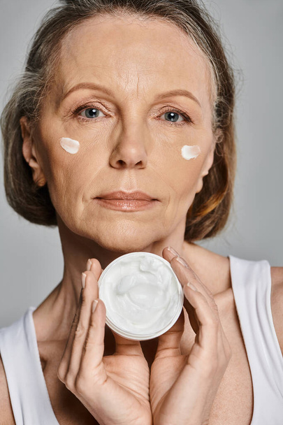 Зрелая женщина мягко наносит крем на лицо. - Фото, изображение
