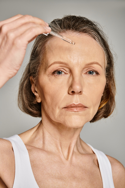 Una donna applica con attenzione un siero sul suo viso, concentrandosi sulla sua routine di cura della pelle.. - Foto, immagini