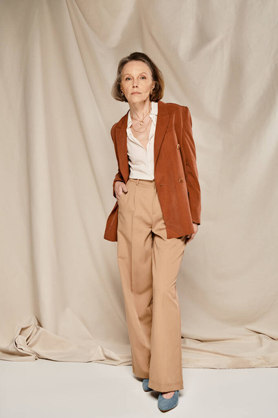 Stilvolle reife Frau in braunem Blazer und Hose, die selbstbewusst und anmutig posiert. - Foto, Bild