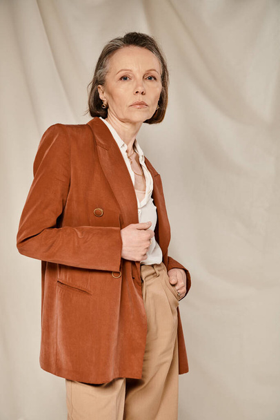 Mujer madura en chaqueta bronceada y pantalones, poses llamativas con confianza y gracia. - Foto, Imagen