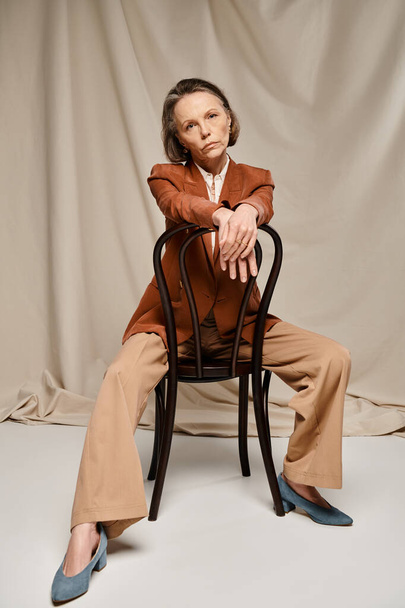 Une femme mature et séduisante s'assoit gracieusement dans un costume bronzé, exsudant élégance et calme. - Photo, image