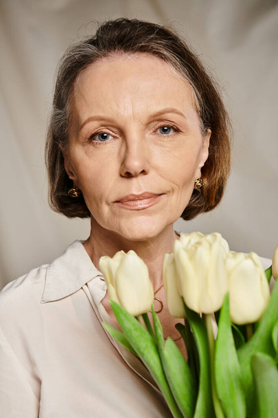 Eine reife Frau hält anmutig einen Strauß weißer Tulpen in der Hand. - Foto, Bild