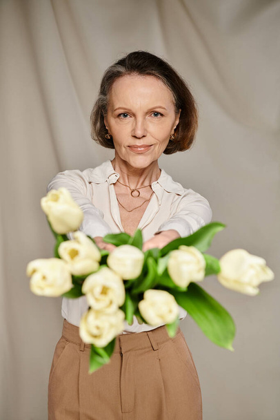 Зріла жінка витончено тримає букет з білих тюльпанів, виключаючи елегантність і витонченість. - Фото, зображення