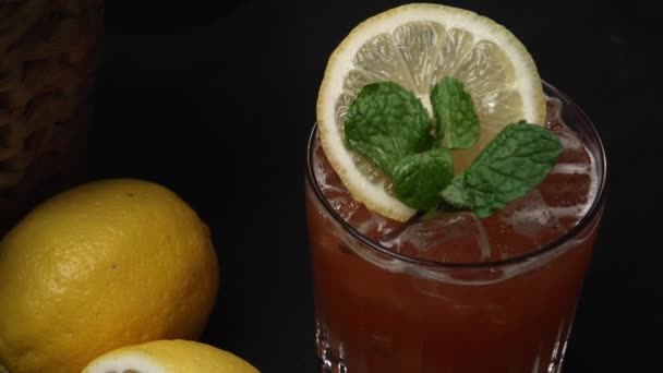 Macrografie, van een Tequila Sunrise cocktail versierd met een schijfje citroen en verse munt verlof, geplaatst tegen een dramatische zwarte achtergrond. Close-up shot vangt de levendige kleuren van cocktail. Bestanddelen. - Video