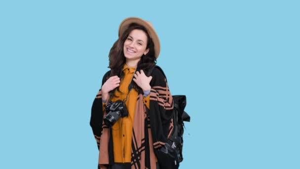 Boldog fiatal nő élvezi utazás közben tartó kamera és hátizsák kék elszigetelt háttérrel. Kirándulás, turizmus, kalandok koncepciója - Felvétel, videó