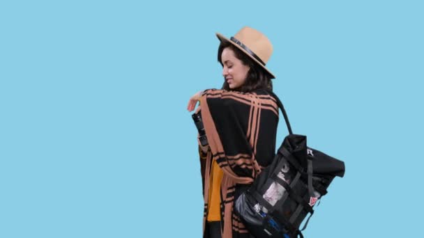 Boldog elegáns nő kalapban hátizsák megy, hogy a fotó kamerával az utazás során a kék elszigetelt háttér. Kirándulás, turizmus, kalandok koncepciója - Felvétel, videó