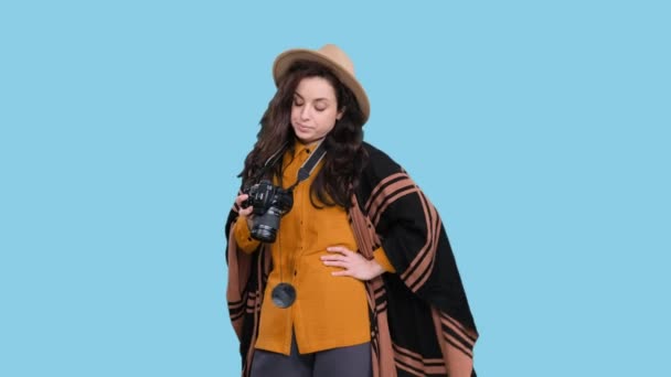 Сумна жінка-фотограф у стильному капелюсі дивиться на екран камери, незадоволена фотографіями на синьому ізольованому фоні. Поїздка, туризм, концепція пригод - Кадри, відео