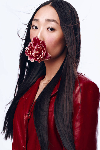 Mujer misteriosa con el pelo largo y negro en chaqueta roja sosteniendo una flor en su boca - Foto, imagen