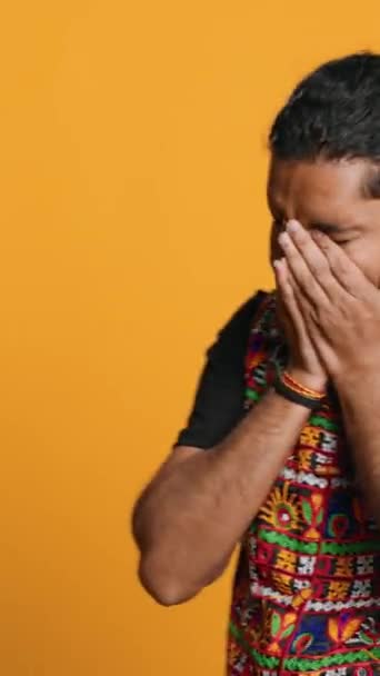 Pystysuora video Intialainen mies peittää kasvot kämmenet epäusko, tunne järkyttynyt tapahtumista, eristetty yli studio tausta. Perattu henkilö kynsien kynsien iholla turhautuneena, ärsyyntynyt huolestuttavia uutisia - Materiaali, video