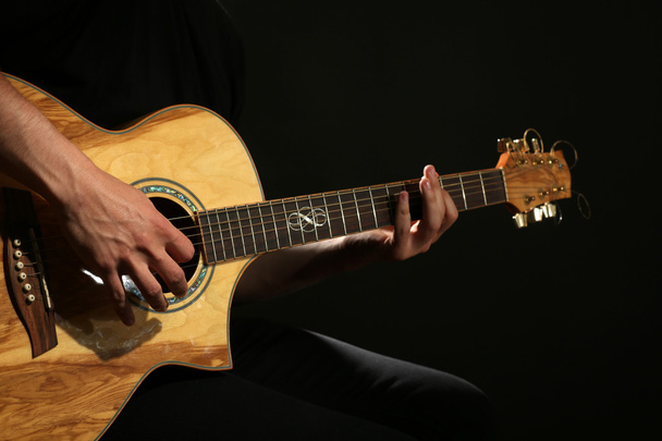 Young man playing on acoustic guitar on dark background - Fotó, kép