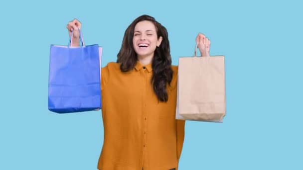 Usmívající se mladá žena si užívá nakupování, zatímco drží papírové sáčky na modrém izolovaném pozadí. Černý pátek, koncept prodeje - Záběry, video