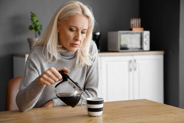 Mujer madura deprimida vertiendo café en la cocina - Foto, Imagen
