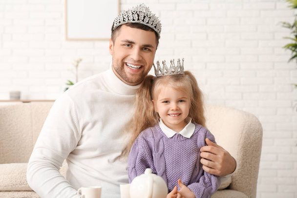 gelukkig vader met zijn schattig dochtertje in prinses kronen het hebben van thee partij thuis - Foto, afbeelding