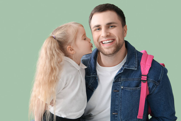 Милая маленькая школьница целует своего счастливого отца на зеленом фоне - Фото, изображение