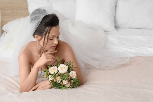 Όμορφη νεαρή νύφη με γαμήλιο μπουκέτο ξαπλωμένη στο υπνοδωμάτιο - Φωτογραφία, εικόνα