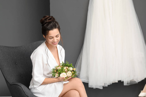 Beautiful young bride with her wedding bouquet sitting in dressing room - Fotó, kép