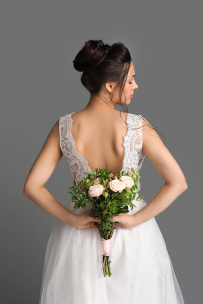 Mooie jonge bruid met bruiloft boeket op donkere achtergrond, achteraanzicht - Foto, afbeelding