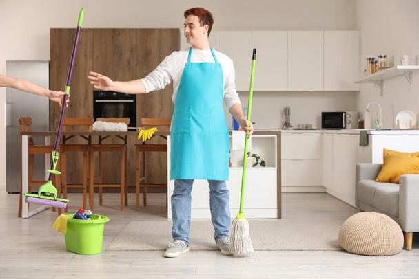 Молодий чоловік бере мокрий підлогу від жінки на кухні - Фото, зображення
