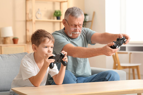 Ο παππούς με τον εγγονό του παίζουν βιντεοπαιχνίδια στο σπίτι. - Φωτογραφία, εικόνα