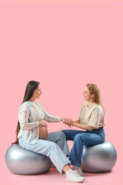 Doula mature avec femme enceinte sur fitballs tenant la main sur fond rose - Photo, image