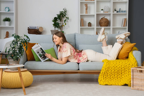Mujer joven leyendo revista en el sofá en la sala de estar - Foto, Imagen