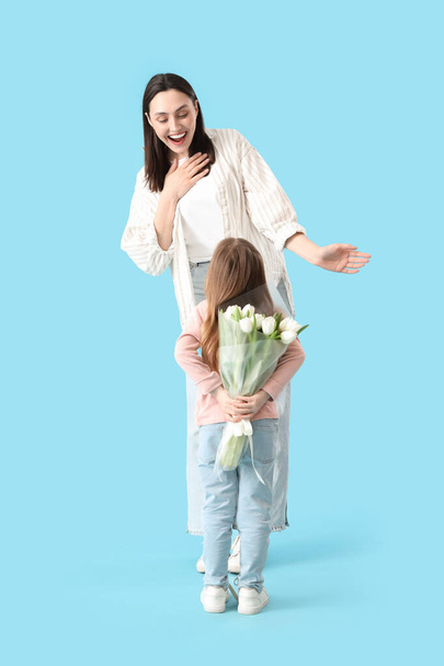 Young woman receiving tulips from her little daughter on blue background. Mother's Day celebration - Photo, Image