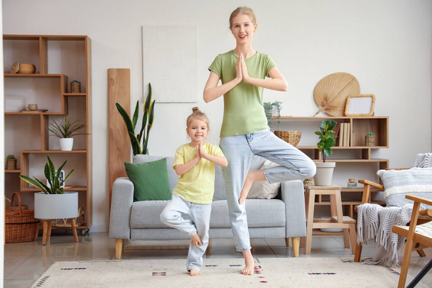 Mooie jonge sportieve vrouw met haar kleine dochter oefenen yoga in de woonkamer - Foto, afbeelding