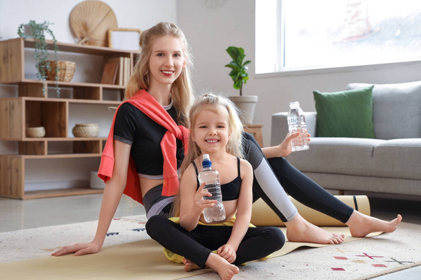 Νεαρή αθλητική γυναίκα με την κορούλα της με μπουκάλια νερό στο σπίτι - Φωτογραφία, εικόνα
