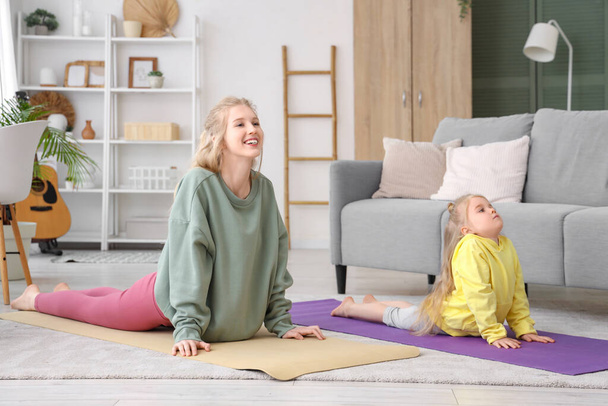 jonge sportieve vrouw met haar dochtertje oefenen yoga in de woonkamer - Foto, afbeelding