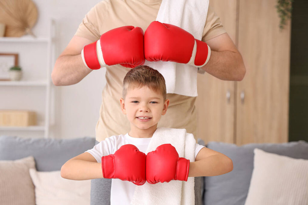 Молодой человек с маленьким сыном в боксёрских перчатках в гостиной - Фото, изображение