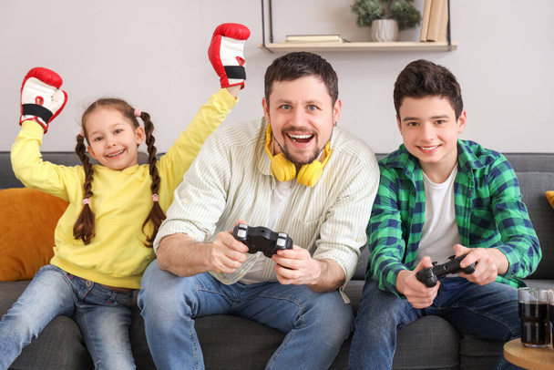 Little girl in boxing gloves with her father and brother playing video game at home - Photo, Image