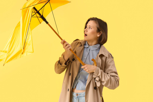 Молодая женщина со сломанным зонтиком и сильным ветром на желтом фоне - Фото, изображение