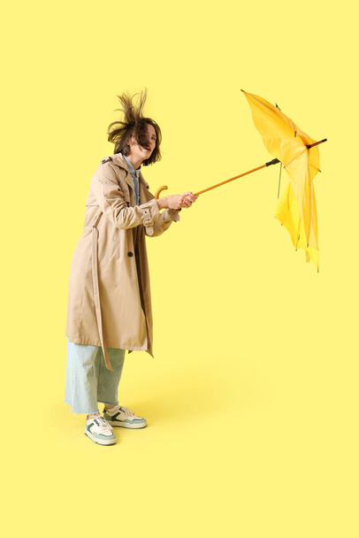 Nuori nainen rikki sateenvarjo ja voimakas tuuli keltaisella taustalla - Valokuva, kuva