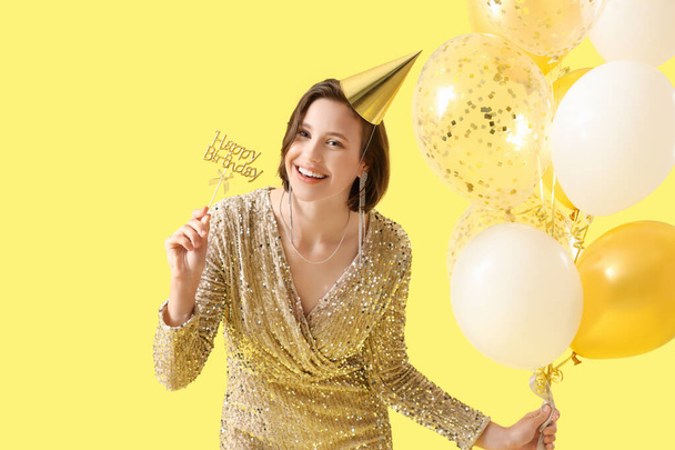 Bella donna in cappello partito con palloncini di compleanno su sfondo giallo - Foto, immagini