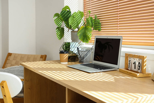 Ordenador portátil con florario y planta sobre mesa en oficina ligera - Foto, Imagen